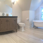 ottawa bathroom renovations Renovated bathroom with white and grey striped floor tile, white painted walls, brown sink cabinet with large frameless mirror and wall mounted lights, and a standalone bathtub with vintage design metal legs.